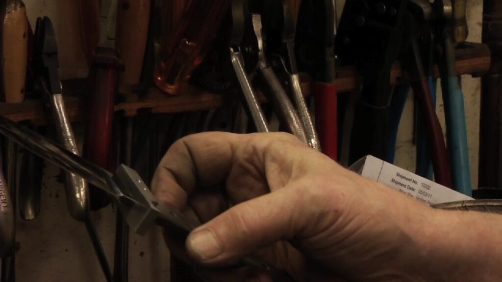 A hand holding unfinished knife blade blanks in the Loveless shop