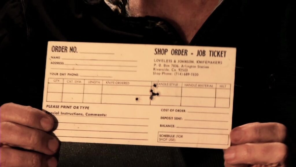 Hands holding a shop order job ticket from the Loveless knife shop